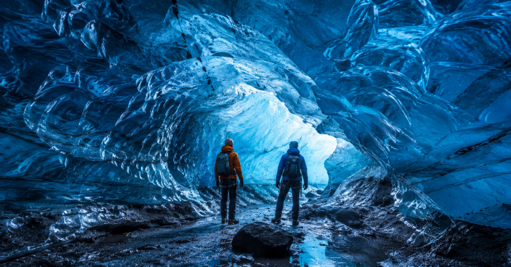 Explorers inside glowing blue Katla ice cave near Vik Iceland with crystal ice walls and dramatic frozen glacier interior