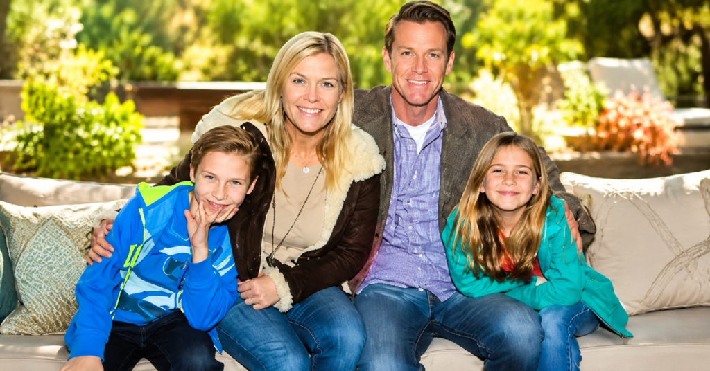 Family portrait of Alison Sweeney, David Sanov, Benjamin Sanov, and Polly Sweeney sitting together outdoors with a bright luxury background in high-quality editorial style.