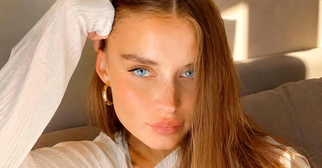 Lola Lovell close-up portrait with blue eyes and soft natural makeup in warm golden sunlight, featured in a premium editorial style banner image.Golden hour glow selfie portraitEdit
