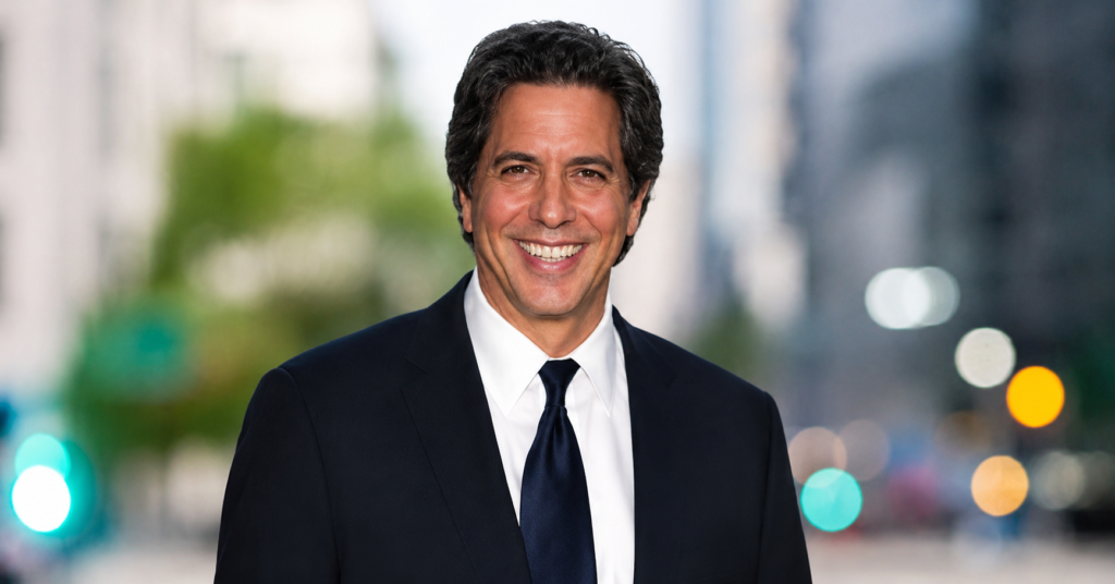 Professional HD portrait of Constantine Yankoglu in a black suit and tie with a blurred modern city background and cinematic bokeh lights.