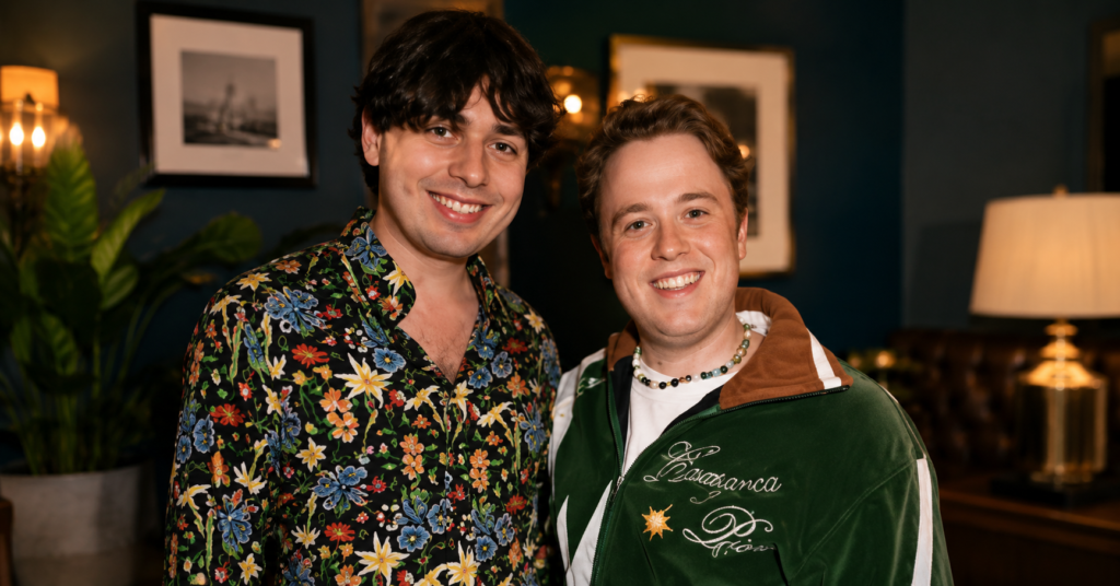 Jordan Sangha and Henry Southan smile together during a social event, posing for a friendly photo in a warmly lit indoor setting.