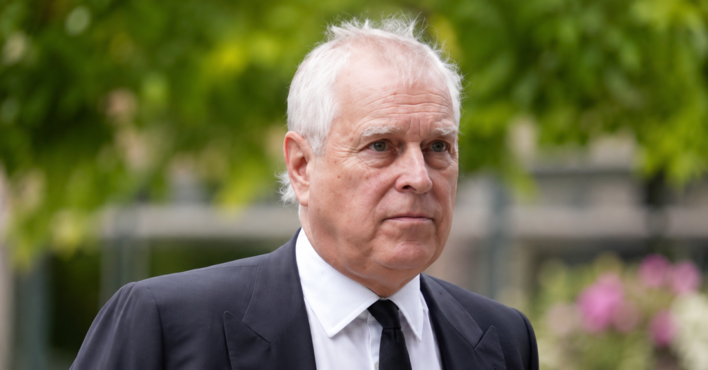Andrew Mountbatten-Windsor in a dark suit and tie during a formal public appearance, photographed outdoors with a blurred green background.