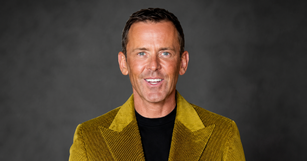 Scott Mills Sacked news topic image showing Scott Mills smiling in a gold blazer and black shirt during a public appearance.