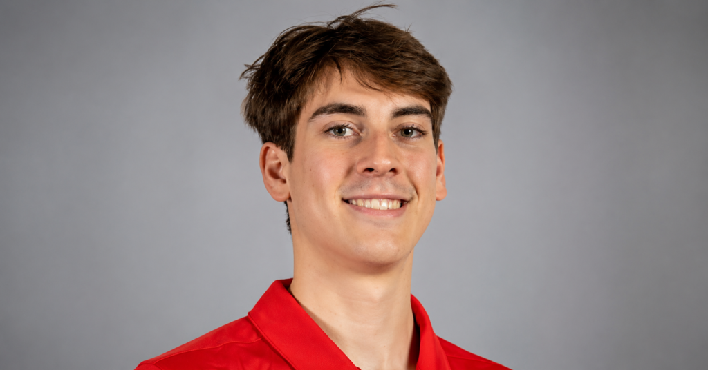 Ryan Grantham smiling in a red polo shirt during a professional portrait session against a neutral background.
