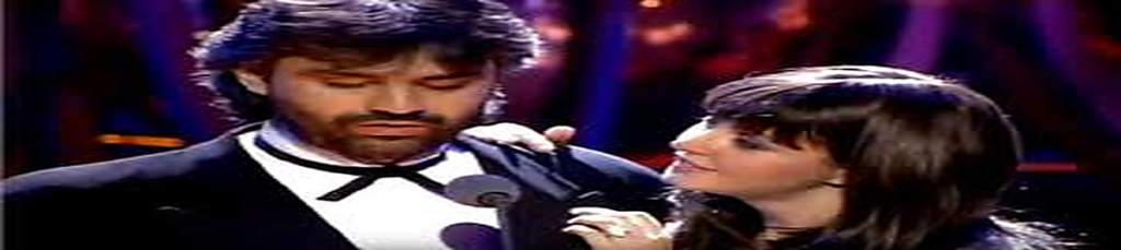 Andrea Bocelli and Sarah Brightman performing “Time to Say Goodbye” on stage during an emotional live duet, dressed in formal attire under warm concert lighting.