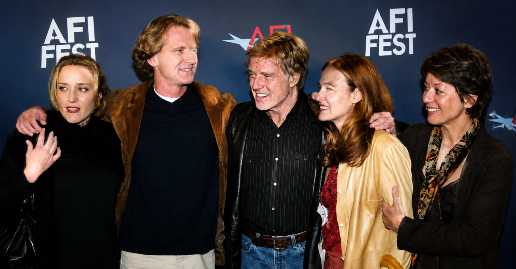 Robert Redford posing with family members at a film festival event, smiling together on the red carpet in front of a modern cinematic backdrop, showcasing a rare family appearance.
