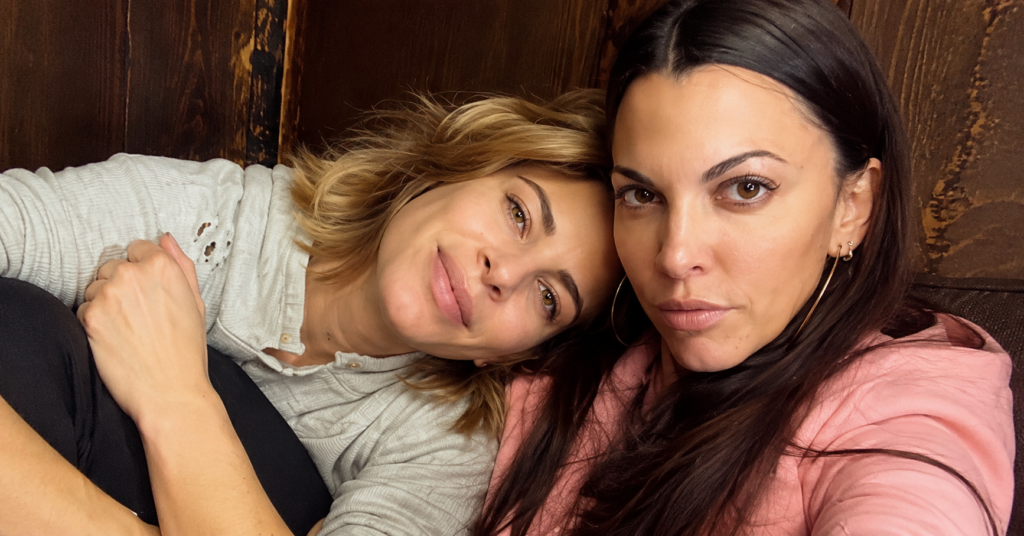 Deshanna Marie Minuto posing with a female companion in a cozy indoor setting, sharing a candid moment in a close-up selfie.