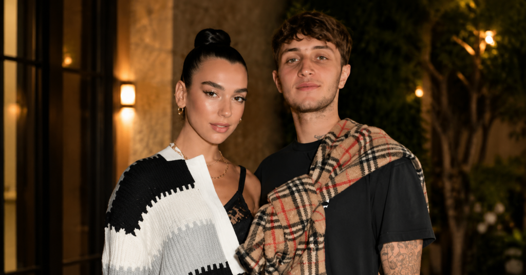 Anwar Hadid posing with a companion at a stylish evening event, wearing a black T-shirt with a plaid scarf draped over his shoulders in a sophisticated outdoor setting.