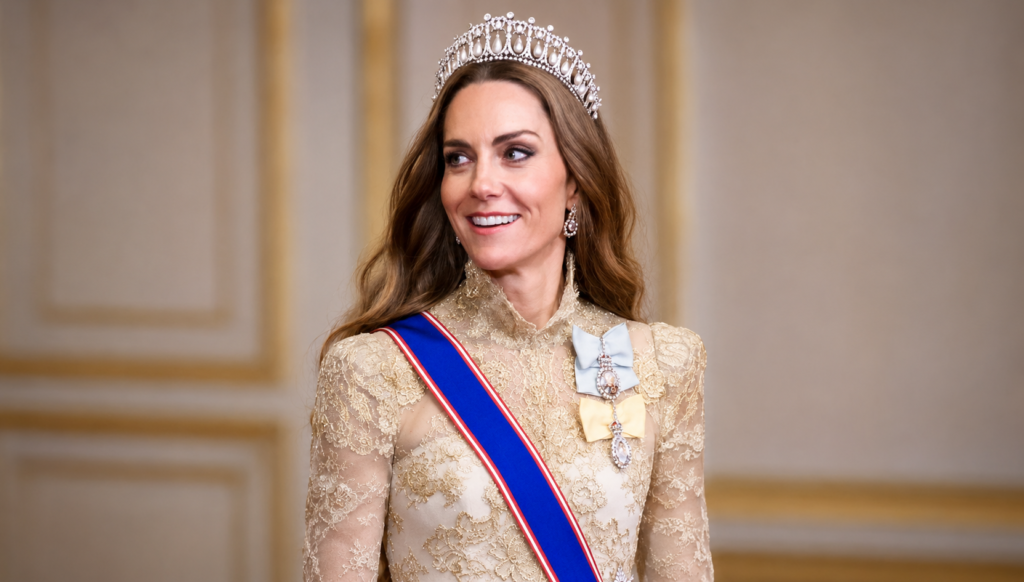 Kate Middleton smiling while wearing a jeweled tiara, an embroidered cream gown, and a blue royal sash during an official royal engagement.