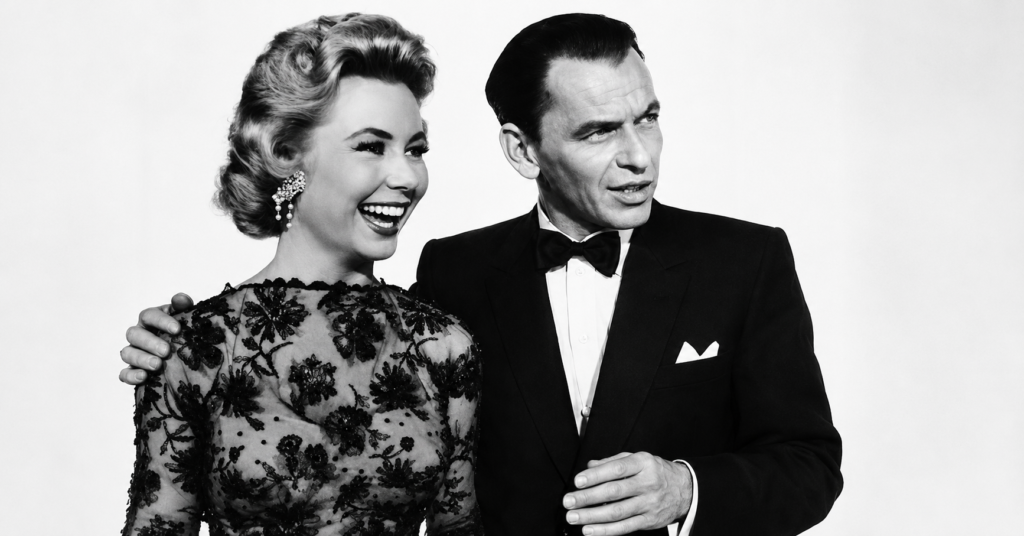Black-and-white publicity photo of Frank Sinatra in a tuxedo standing beside Mitzi Gaynor, who is smiling in an elegant lace evening dress, from the 1957 film The Joker Is Wild.