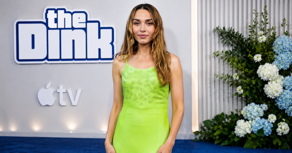 Chloe Fineman posing on the blue carpet at The Dink premiere, wearing a sleeveless lime green dress in front of an Apple TV+ and The Dink backdrop.