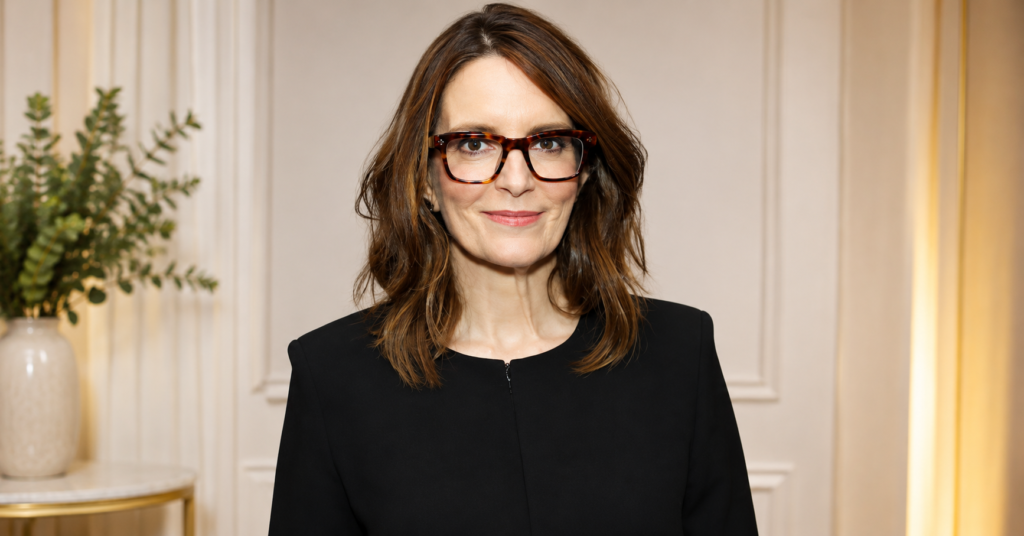 Tina Fey wearing black attire and glasses while posing in front of a SAG-AFTRA Foundation backdrop at a public event.