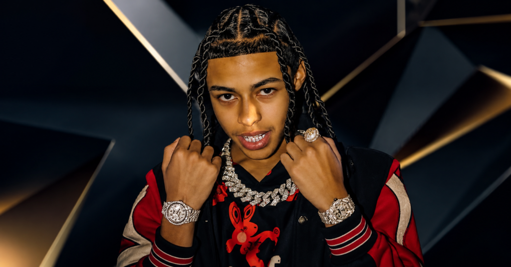 DD Osama wearing a red and black outfit with diamond jewelry, posing confidently for the camera.