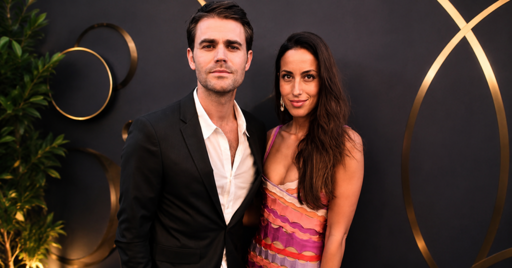 Ines de Ramon stands beside Paul Wesley on the red carpet at a Mercy For Animals event, wearing a colorful patterned dress while he wears a black suit with an open-collar white shirt.