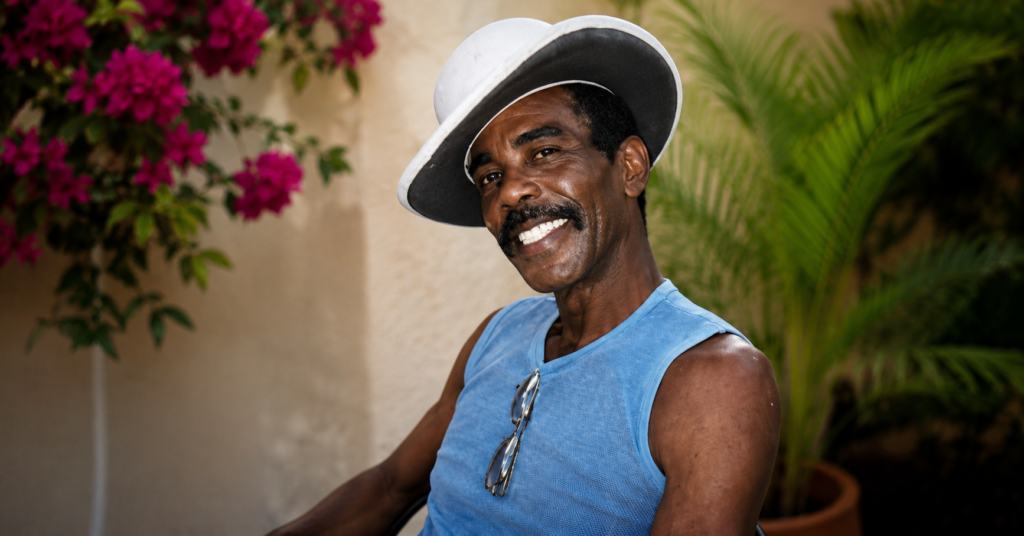 Vintage portrait of Charles Wayne Hendricks smiling while wearing a white hat and blue sleeveless shirt outdoors.