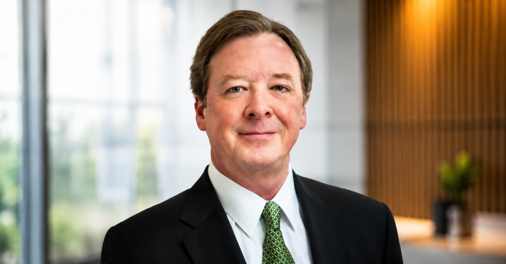 Professional headshot of Robert W. Kirk wearing a black suit, white dress shirt, and green tie against a neutral background.