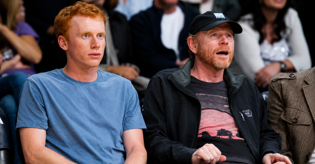 Reed Cross Howard and Ron Howard sitting courtside at a sporting event, watching the game with focused expressions.